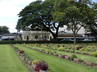 墓石が並ぶ「連合軍共同墓地」。墓地の塀越しに見える白い建物が「泰緬鉄道博物館」（筆者撮影）