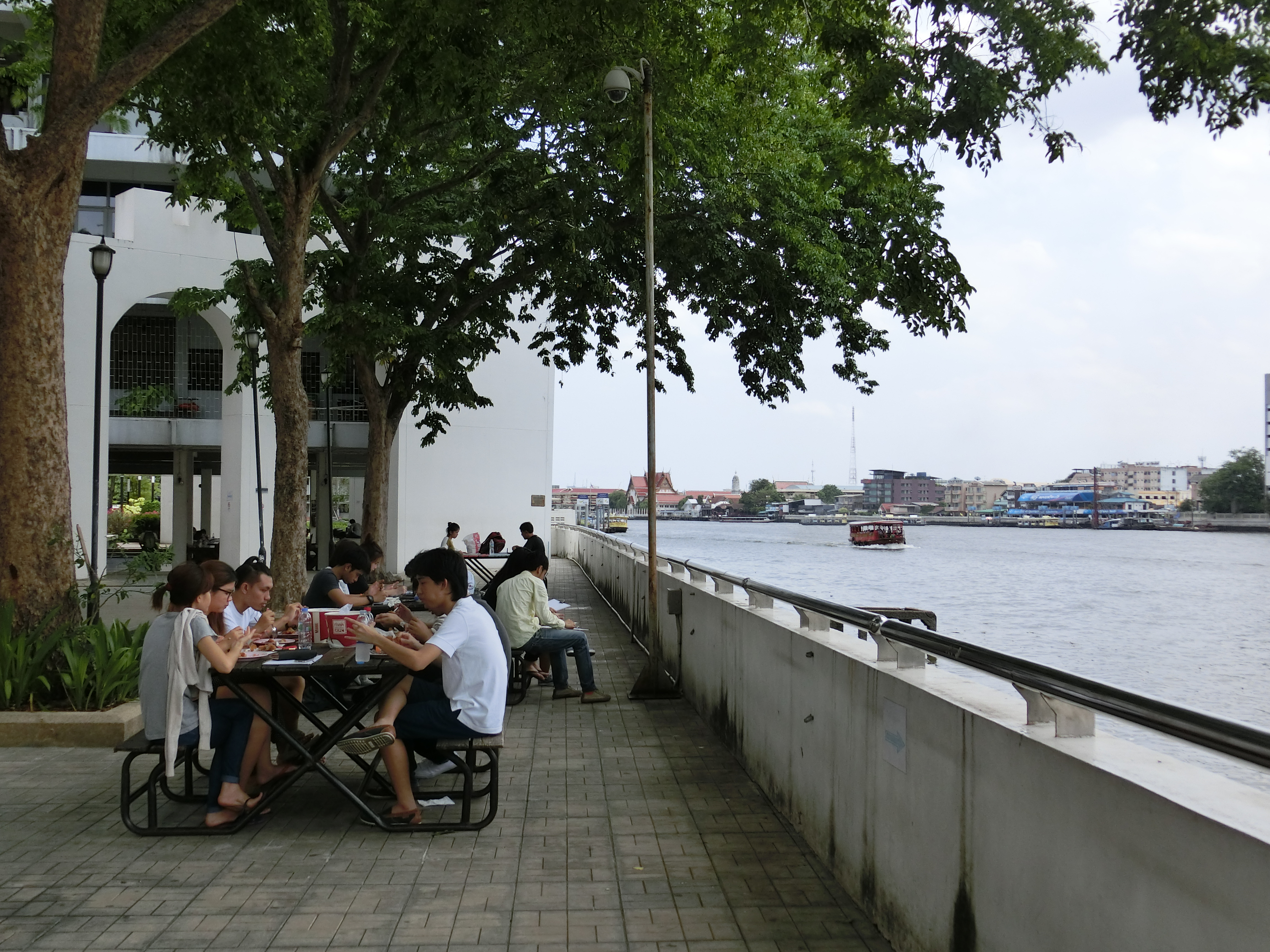 チャオプラヤー川沿いにある、タマサート大学（タープラチャン・キャンパス）の風景。付近の学生食堂で調達した食事を屋外のテーブルに運び、 ランチ中のグループ（2015年、筆者撮影）