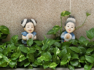 バンコクのタマサート大学（タープラチャン・キャンパス）構内の植え込みで微笑み、ワイをする人形（筆者撮影）
